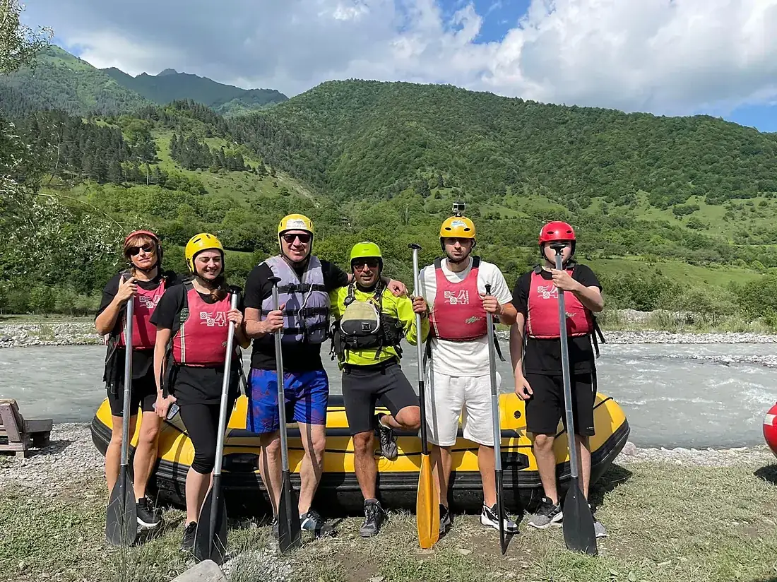 Group posing with paddles in front of a raft