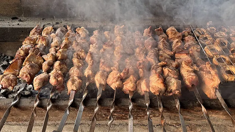 Rows of mtsvadi skewers grilling over coals at the riverside camp